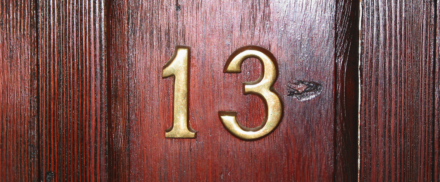 Close-up of brass numbers on a maple wooden door. Apartment 13.