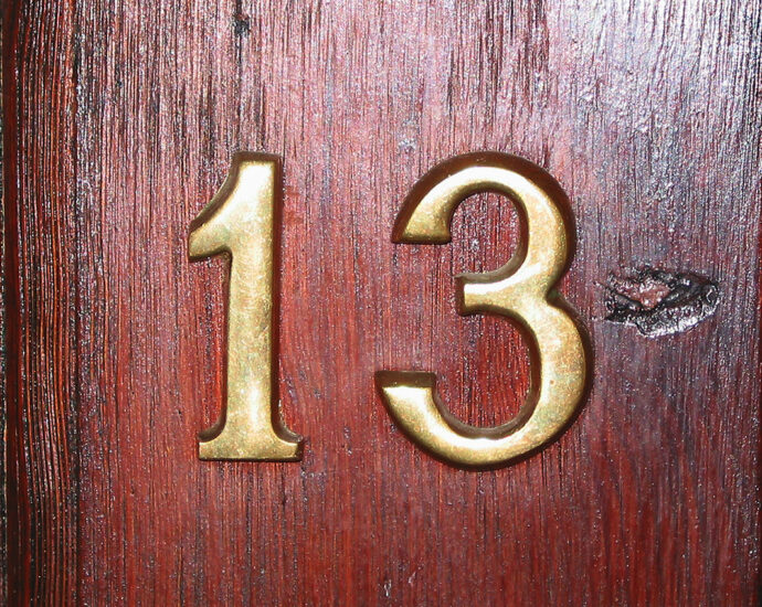 Close-up of brass numbers on a maple wooden door. Apartment 13.