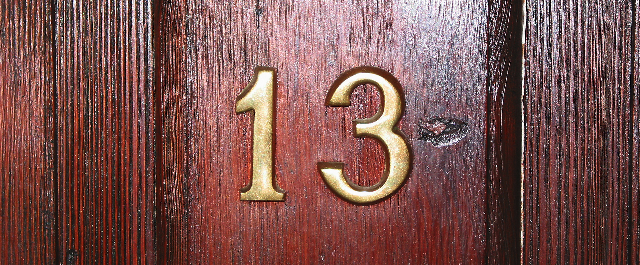 Close-up of brass numbers on a maple wooden door. Apartment 13.