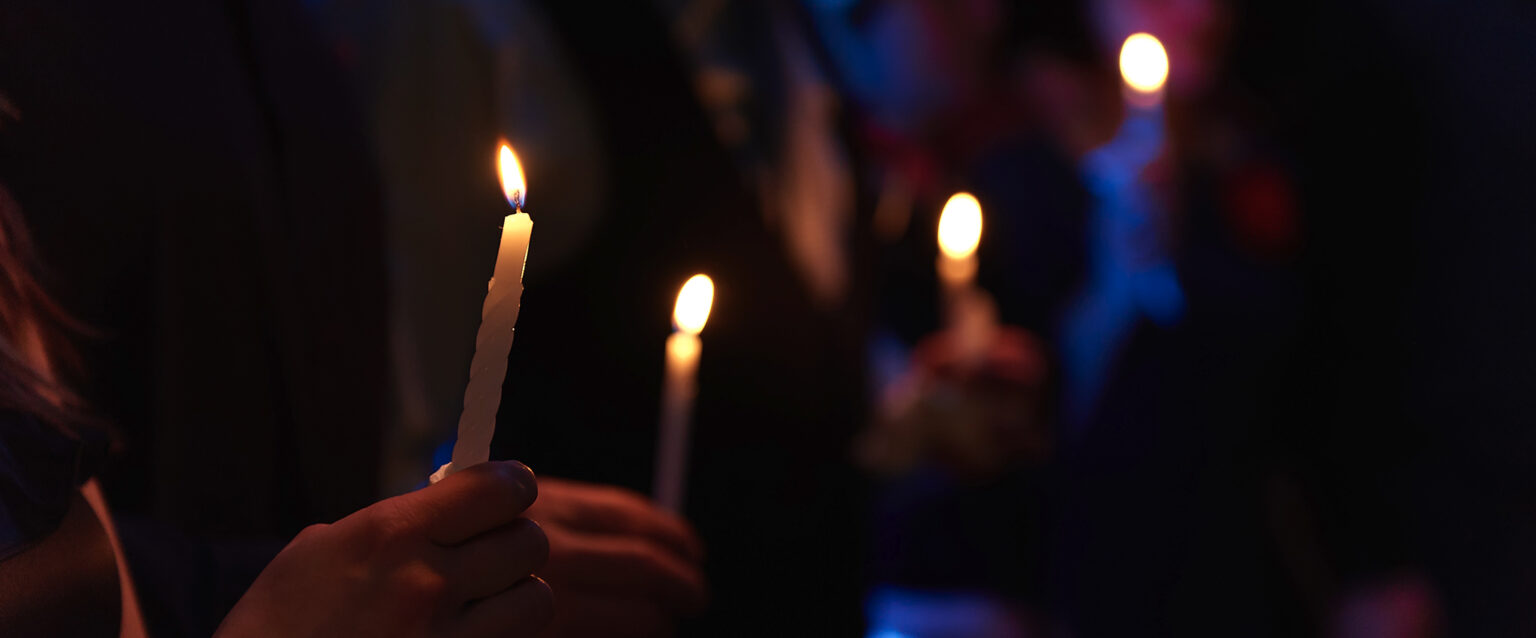 People holding lit candles in a night scene.