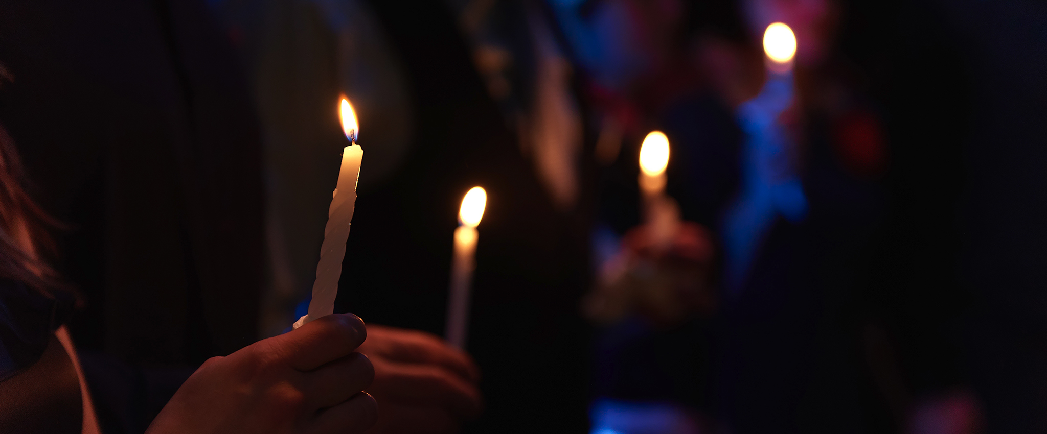 People holding lit candles in a night scene.