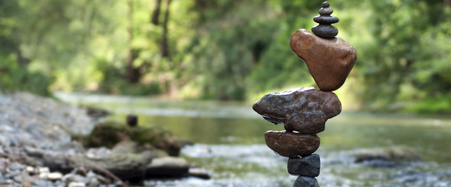 A precariously balanced stack of stones sits beside a small creek in the woods.