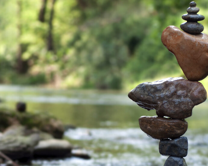 A precariously balanced stack of stones sits beside a small creek in the woods.
