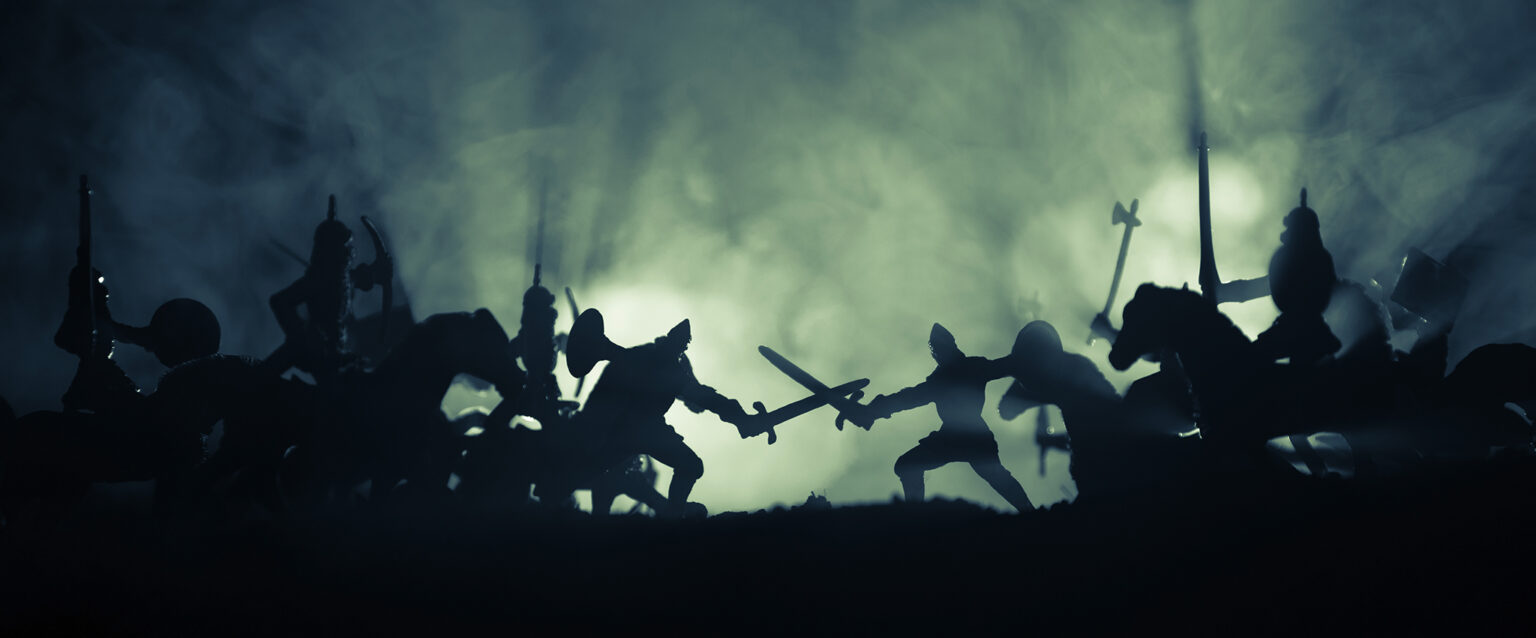 A fog-covered, back-lit Medieval battle scene, in silhouette, with cavalry and infantry.
