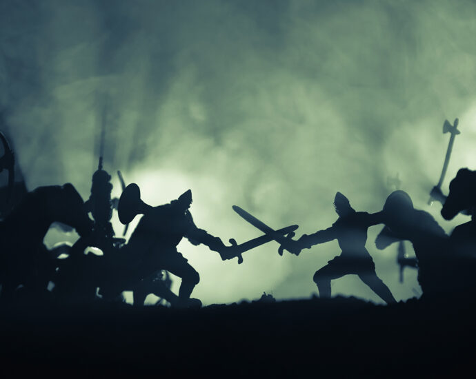 A fog-covered, back-lit Medieval battle scene, in silhouette, with cavalry and infantry.