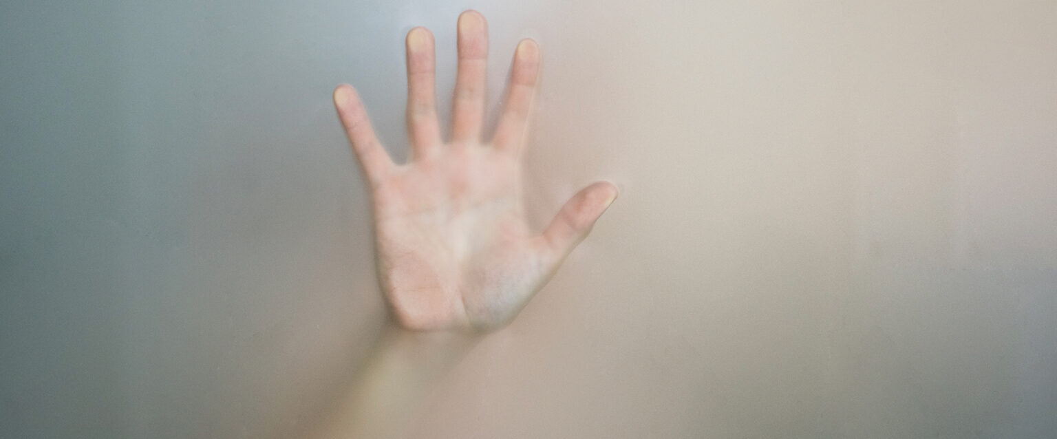 A woman's hand pressed against the glass, reaching out from within the fog.