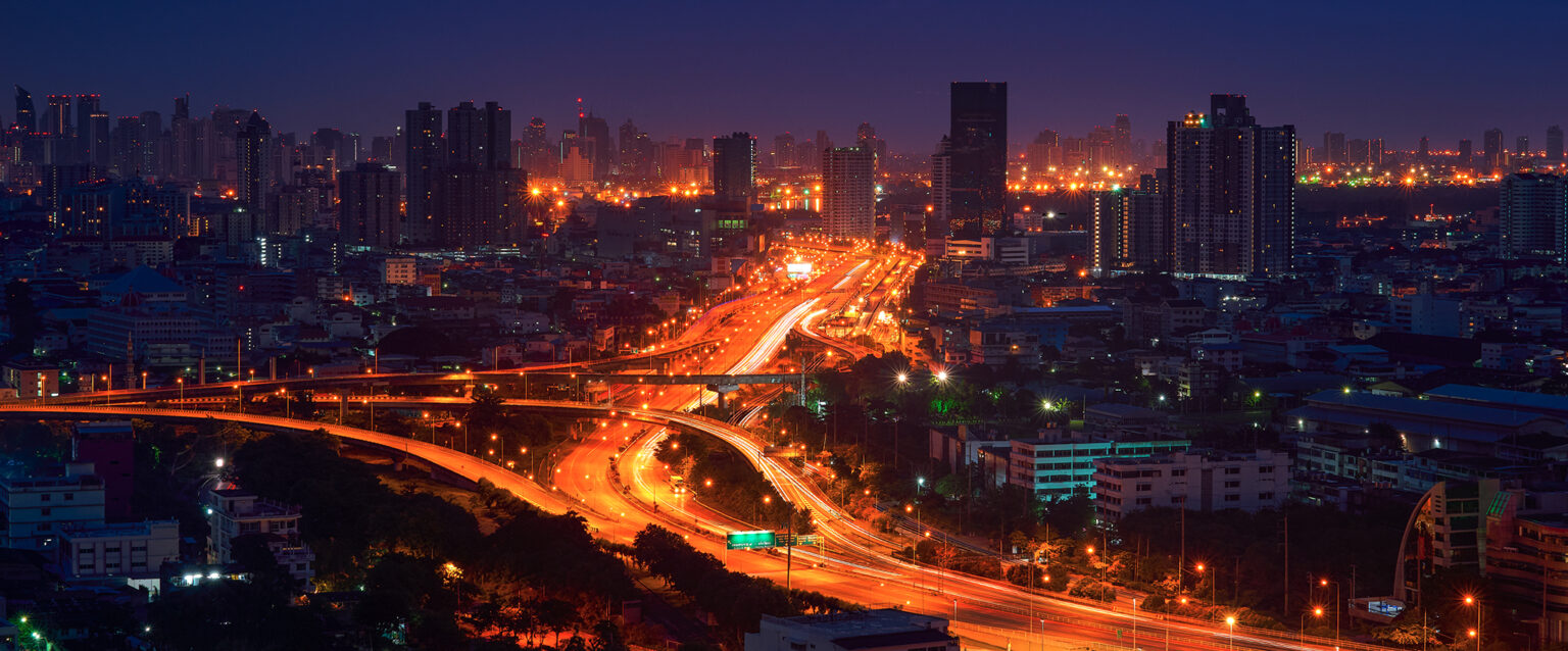 The golden glow of illuminated freeway ramps at night, with headlight and taillight trails of white and red. A time-lapse image.