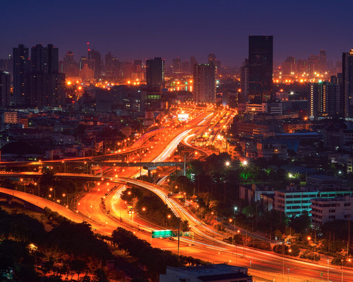 The golden glow of illuminated freeway ramps at night, with headlight and taillight trails of white and red. A time-lapse image.