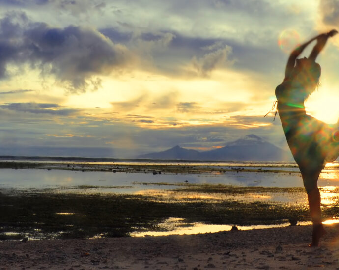 A woman dancing at the beach as the sun goes down over Bali, as seen from Gili, Indonesia.