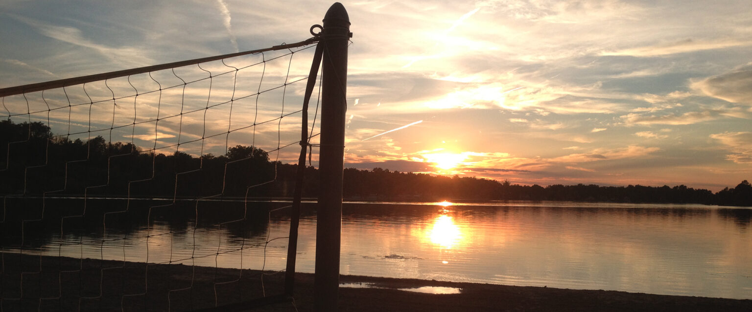 A volleyball net at sunset on a lakefront beach.