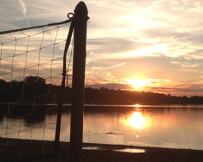 A volleyball net at sunset on a lakefront beach.