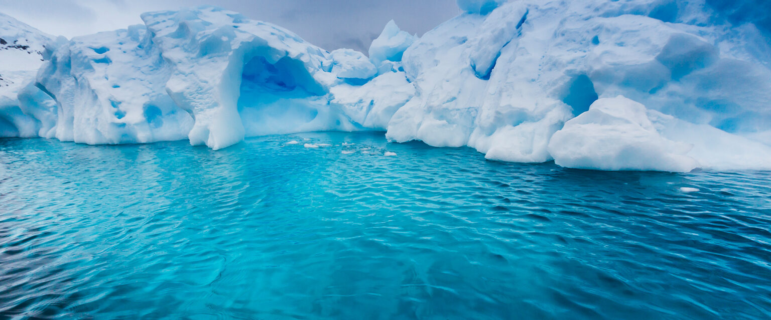 The hidden underside of a large glacier is visible through the turquoise waters of Antarctica.