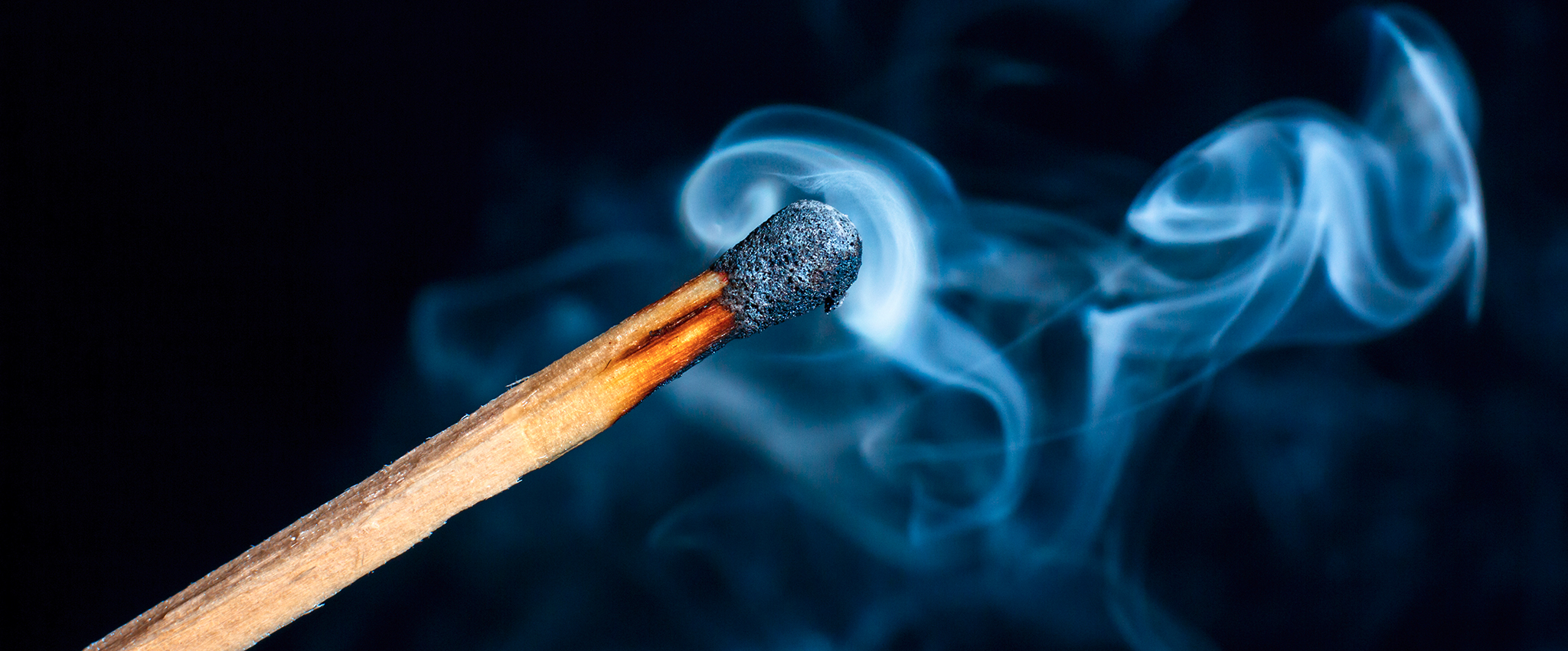 Billows of smoke still flow from the head of a thoroughly burnt wooden match.
