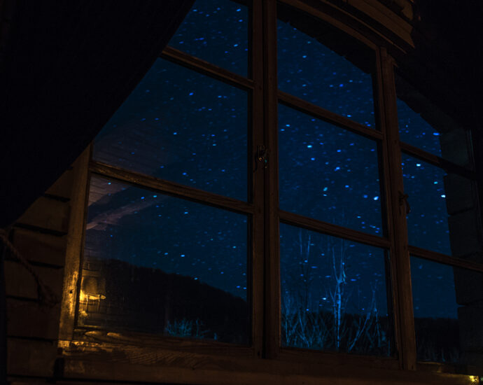 Looking out from within a darkened room, the indigo night sky is aglow, littered with stars.
