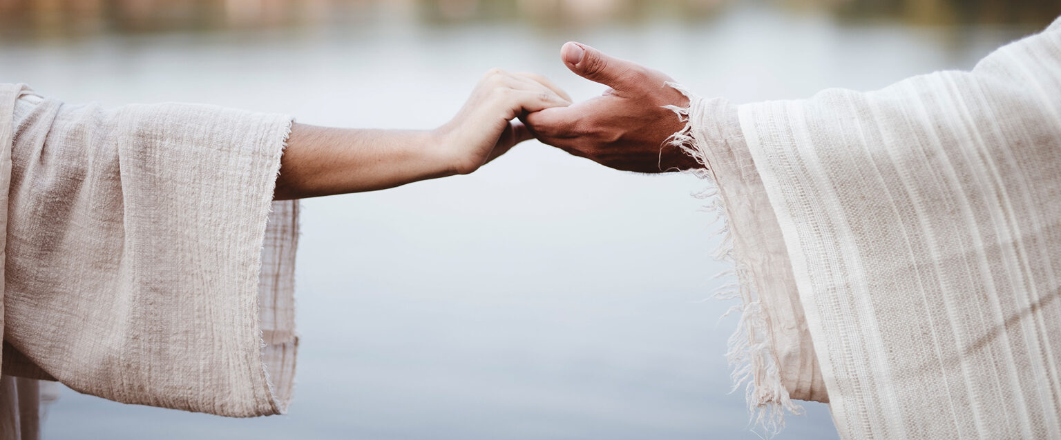 A woman and a man, wearing lightweight robes, reach out to take each other's hands.