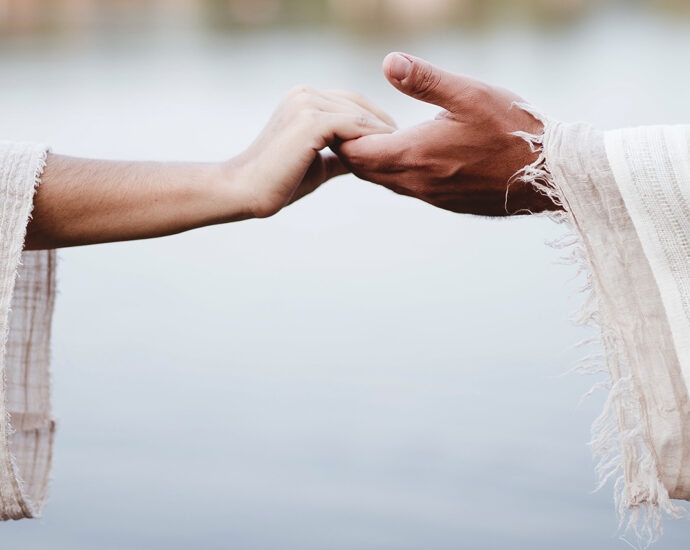 A woman and a man, wearing lightweight robes, reach out to take each other's hands.
