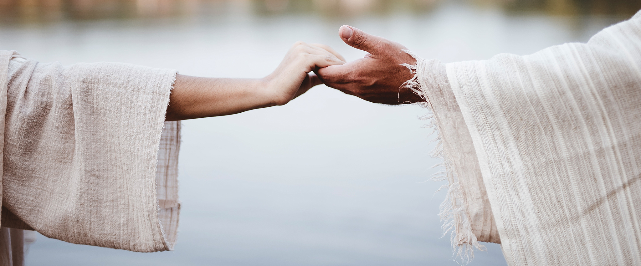 A woman and a man, wearing lightweight robes, reach out to take each other's hands.