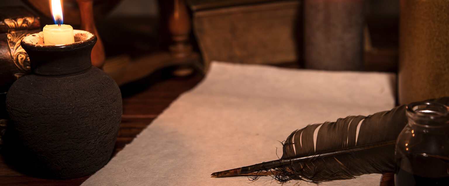 Old parchment paper, a quill, and an ink bottle sit atop a wooden desk, creating a medieval-themed writer's space.
