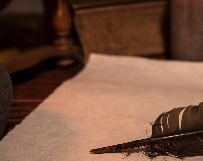 Old parchment paper, a quill, and an ink bottle sit atop a wooden desk, creating a medieval-themed writer's space.