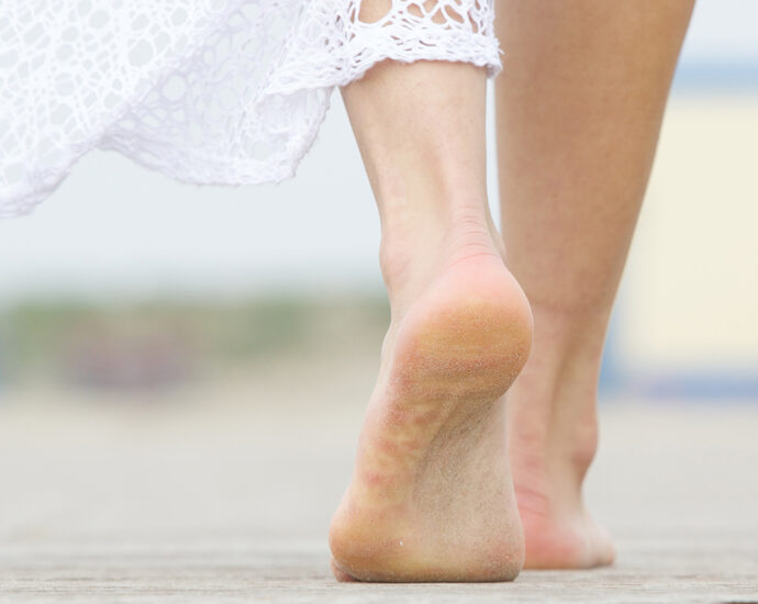 A close-up, low-angle photograph of a barefoot woman, in a white lace dress, walking away.