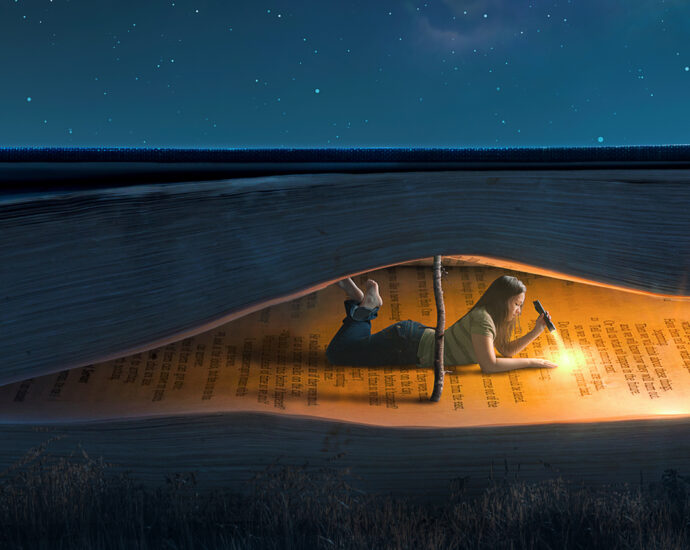 A young woman lies inside a large book, using a branch to prop it open, and reads by flashlight under a night sky.