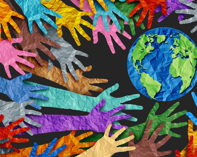 Paper cut-outs of people's arms and the Earth. Each of the pieces is wrinkled, and the arms overlap each other. The arms are cut from many different colors of paper, which is reflective of the diversity of the human race. The Earth is cut from blue and green papers. All of the hands are pointed inward, toward the Earth.
