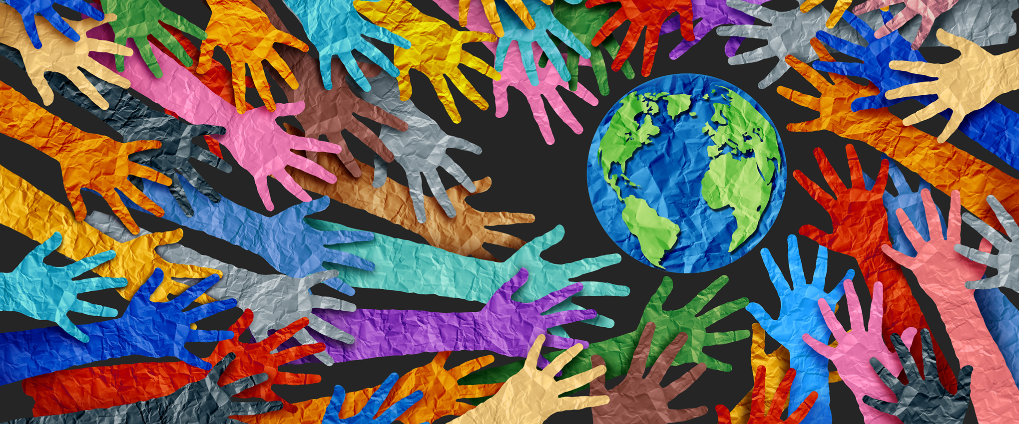 Paper cut-outs of people's arms and the Earth. Each of the pieces is wrinkled, and the arms overlap each other. The arms are cut from many different colors of paper, which is reflective of the diversity of the human race. The Earth is cut from blue and green papers. All of the hands are pointed inward, toward the Earth.