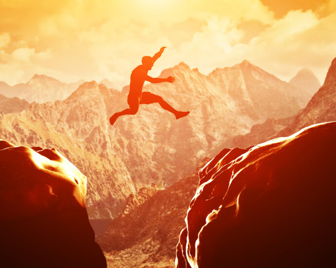 A man jumps over a divide between two rocky mountains at sunset. Freedom, risk, challenge, success.