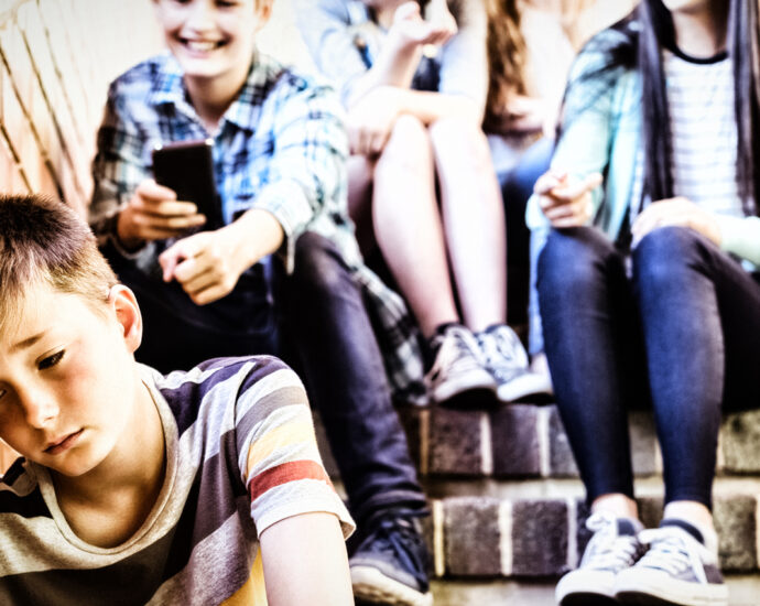 School kid bullies sit on a brick stairway above a boy who is seated, with his head against a brick wall. The victim's expression shows feelings of rejection and ridicule.