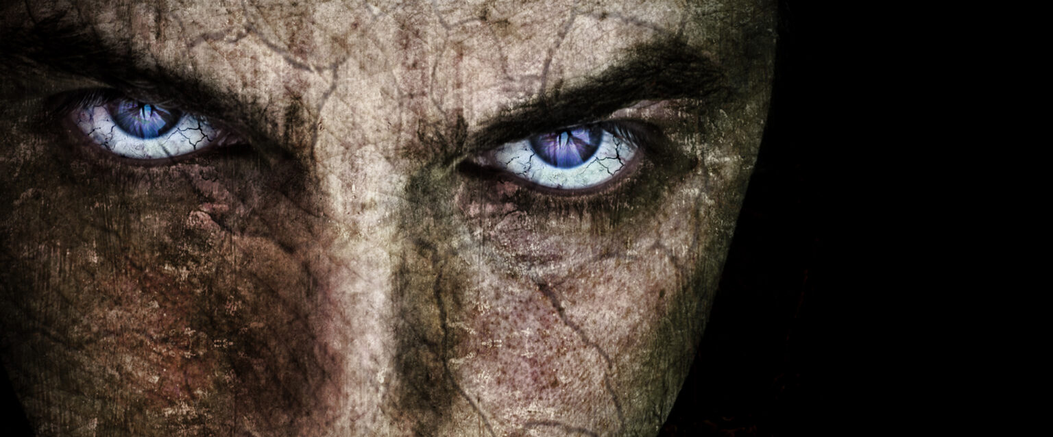 A close-up of a sinister-looking man's face, with cracked skin and purple-blue eyes.