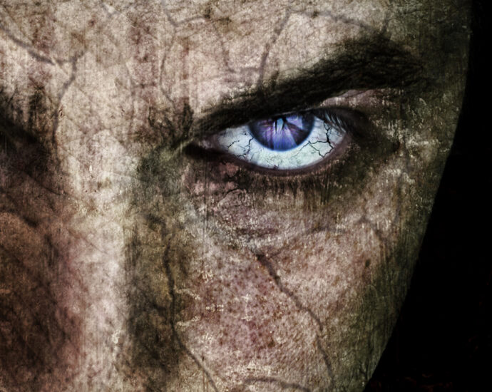 A close-up of a sinister-looking man's face, with cracked skin and purple-blue eyes.