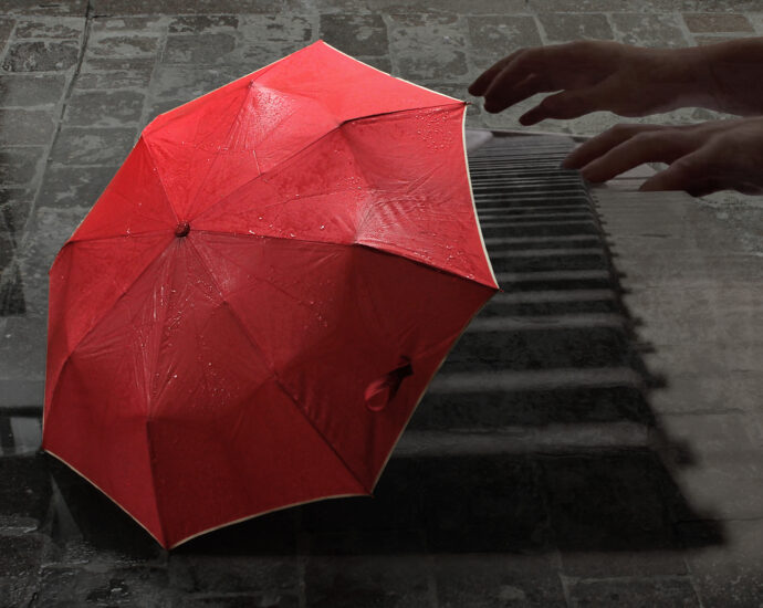 A bright red umbrella site alone on an aged European, wet, gray brick street. Overlay of pianist playing piano.