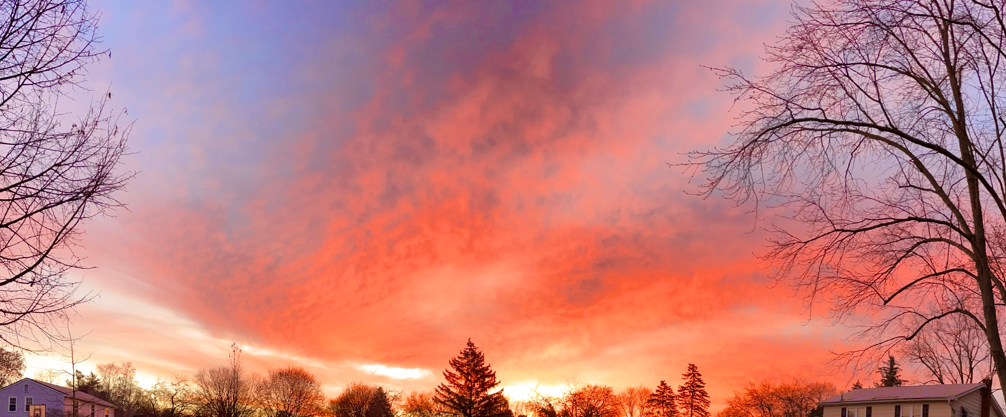 The beautiful red and gold shimmerings of the rising sun streak across the stippled clouds, contrasting with the iridescent blue morning sky.