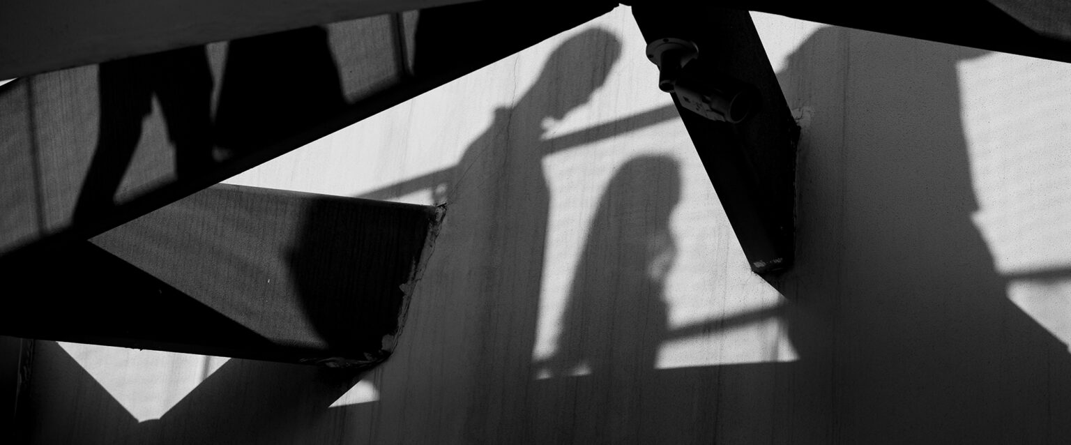 Shadows on a wall, cast by people walking by. Abstract silhouettes amongst large wooden beams.