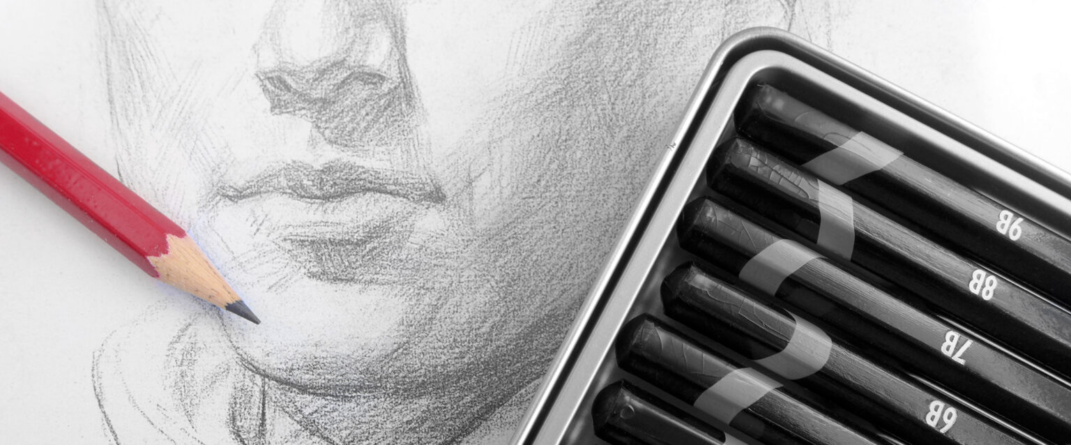 A pencil sketch of a man's face. A tin of numbered, black sketching pencils and a single red pencil lay across the art.