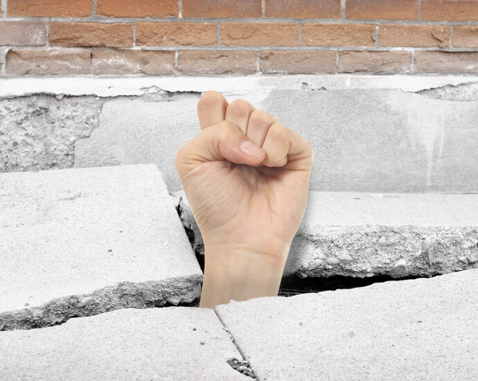 Cracked sidewalk concrete with a woman's fist breaking through from below.