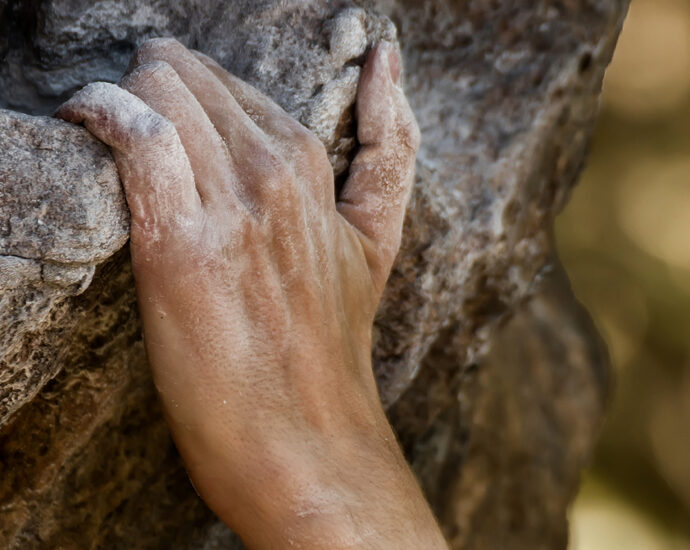 A close-up view of a rock climber's hand gripping a handhold on a natural cliff outcropping