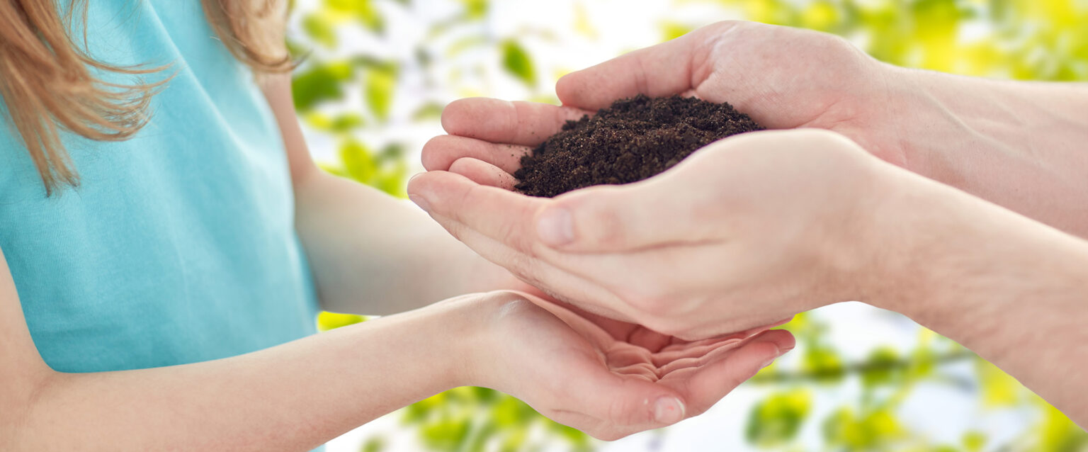 A close-up photo of a man handing a handful of soil to a girl, who has her hands cupped just below his.