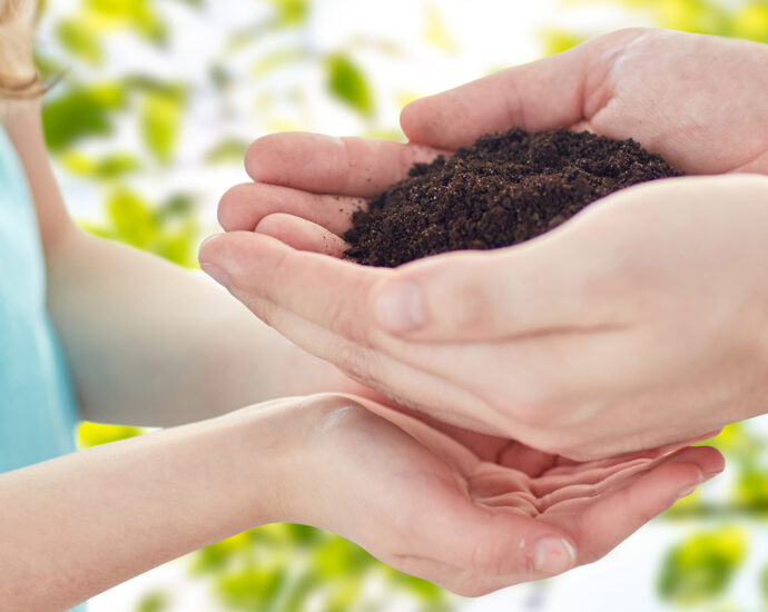 A close-up photo of a man handing a handful of soil to a girl, who has her hands cupped just below his.