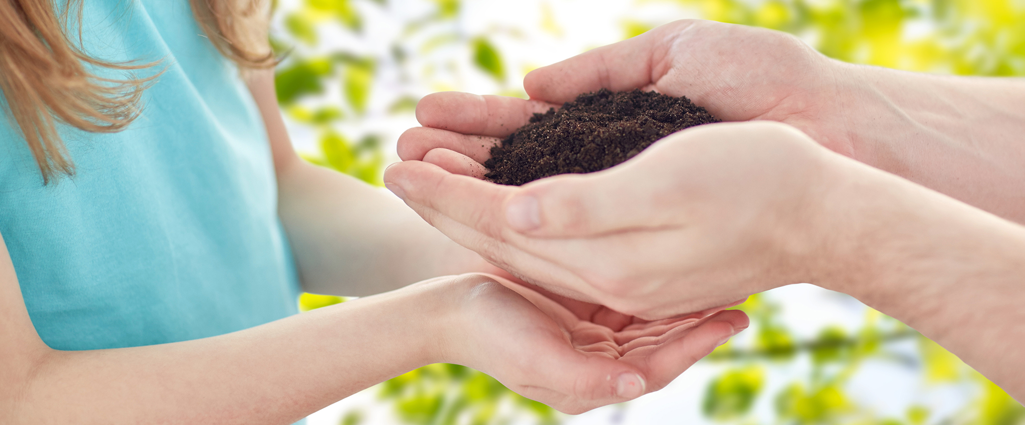A close-up photo of a man handing a handful of soil to a girl, who has her hands cupped just below his.