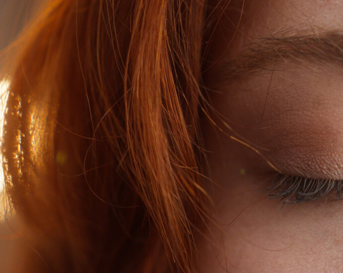 A close-up photo of the right side of the front of a redheaded caucasian woman's face with her eye closed, blinking.