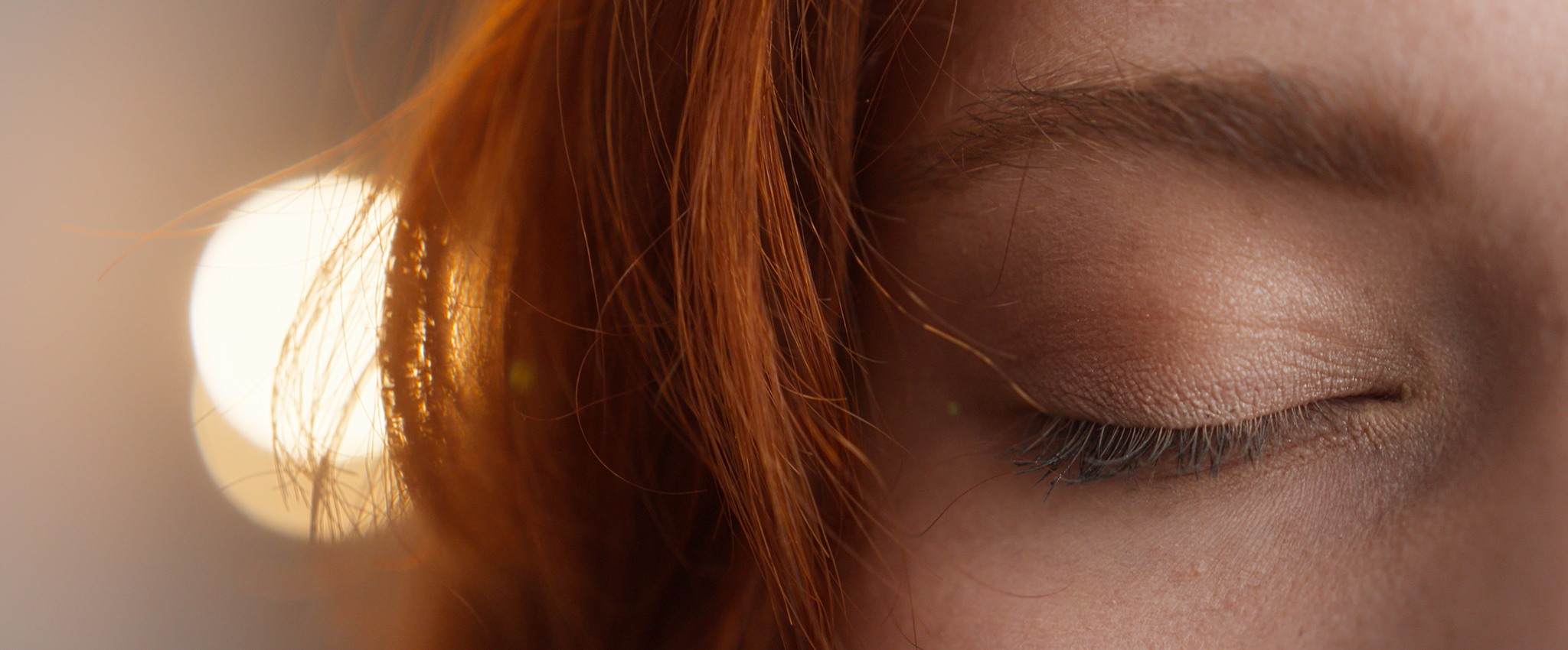 A close-up photo of the right side of the front of a redheaded caucasian woman's face with her eye closed, blinking.