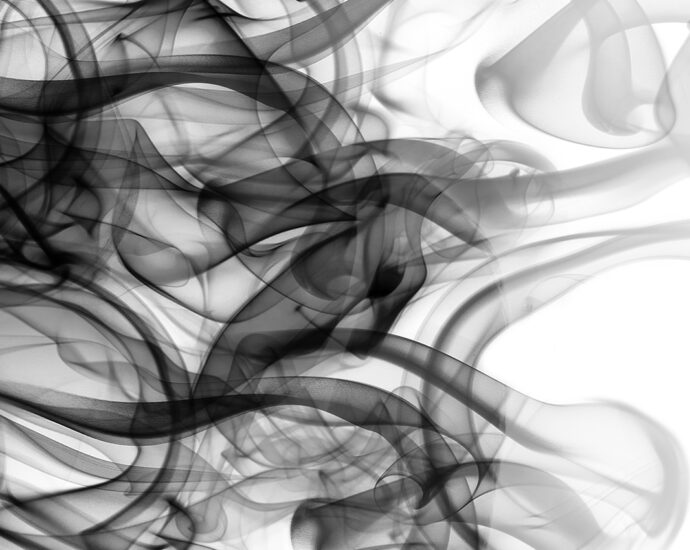 Black smoke in the shape of a side portrait of a woman's face. The black tendrils of smoke create the feeling of long wavy hair blowing in the wind. Double exposure.