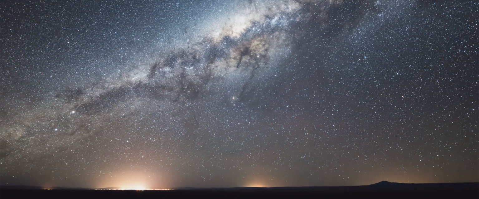 The glow of a distant city beneath a desert sky full of stars.