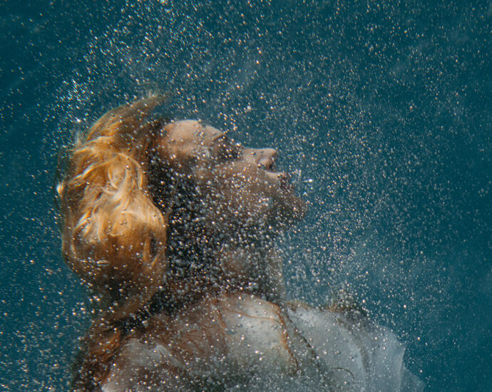 Surrounded by tiny bubbles, a woman in her bridal dress sinks deep beneath the surface of the water.