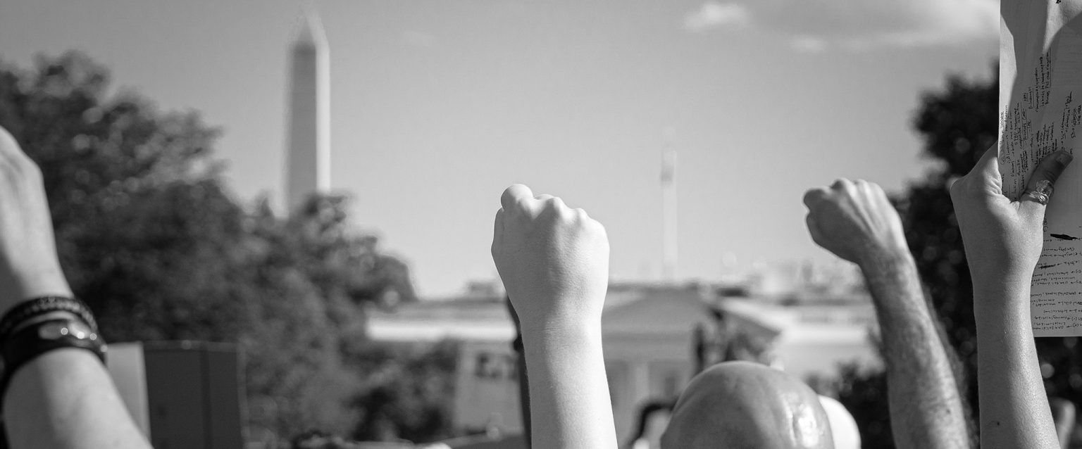 A black and white photo of people, fists raised, protesting in front of the White House, Washington, DC. Taken May 30th, 2020, at a Black Lives Matter rally.