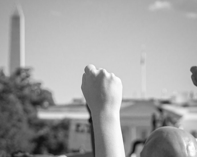 A black and white photo of people, fists raised, protesting in front of the White House, Washington, DC. Taken May 30th, 2020, at a Black Lives Matter rally.