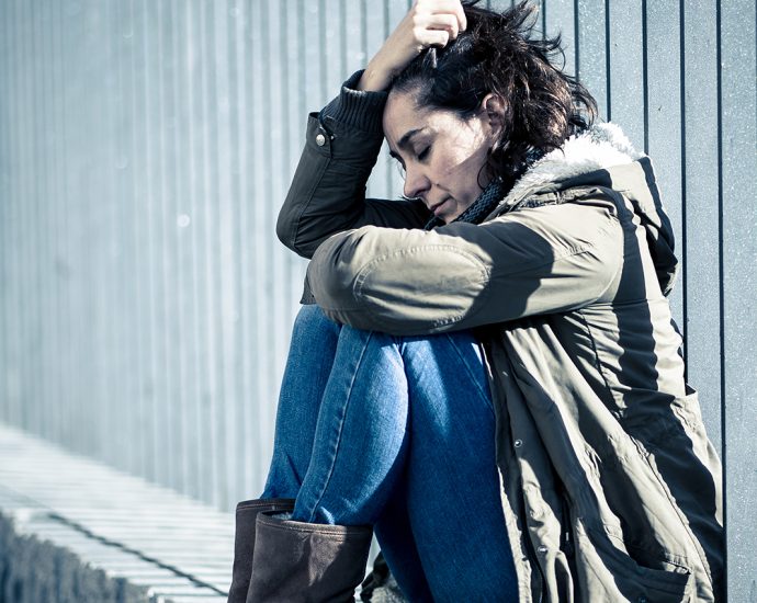 A sad, young woman sits on a cement ledge, contemplating. Abusive relationship and harassment concept