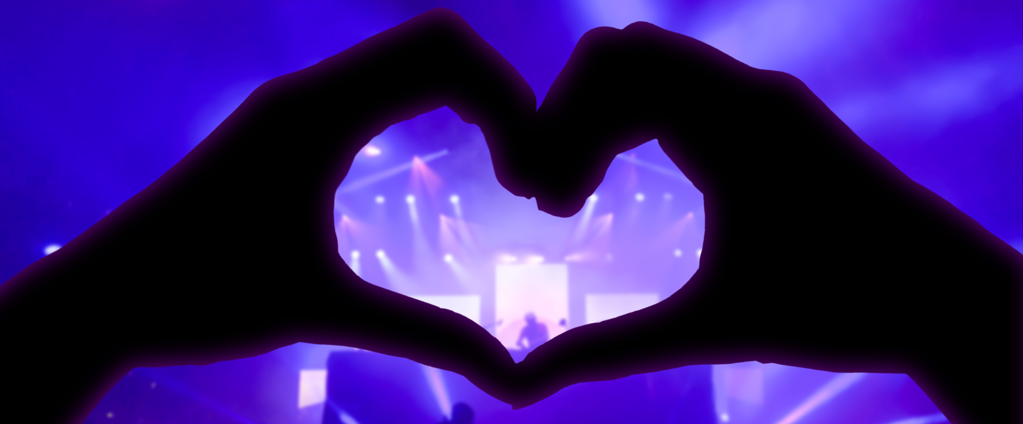 Music concert, hands raised in the shape of the heart for the music, blurred crowd and artists on stage in the background with blue spotlights